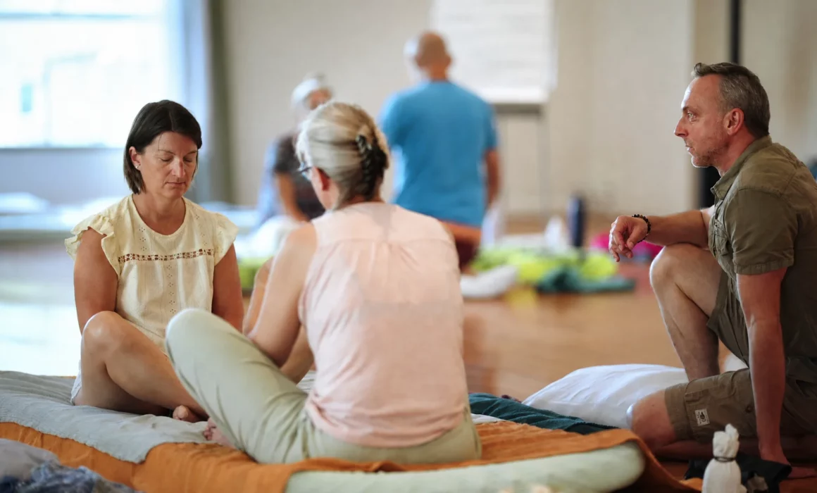 Adultes réunis sur des tapis et des coussins dans un espace de pratique en intérieur.